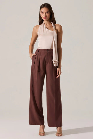 Woman wearing a light pink halter top and brown wide-leg pants on a plain background