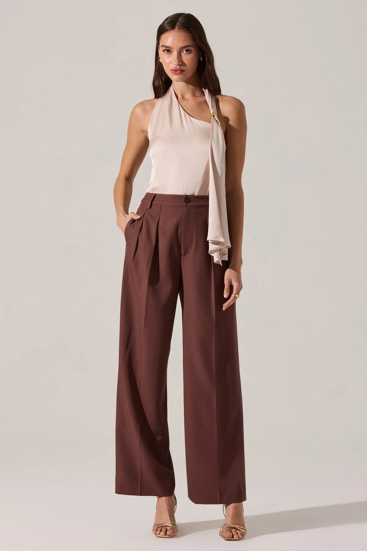 Woman wearing a light pink halter top and brown wide-leg pants on a plain background