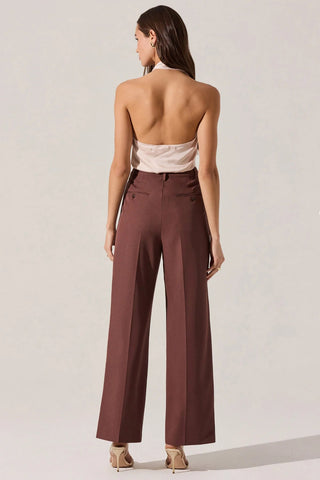 Woman wearing a white top and brown high-waisted pants on a plain background