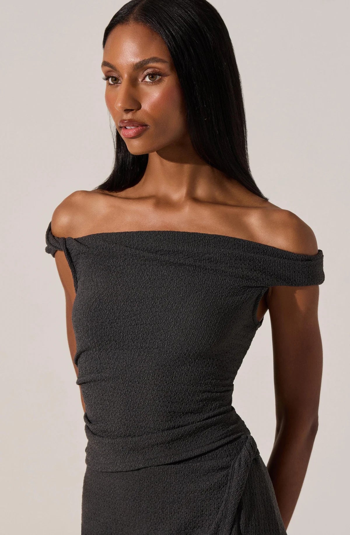 Woman wearing a black off-shoulder dress against a plain background