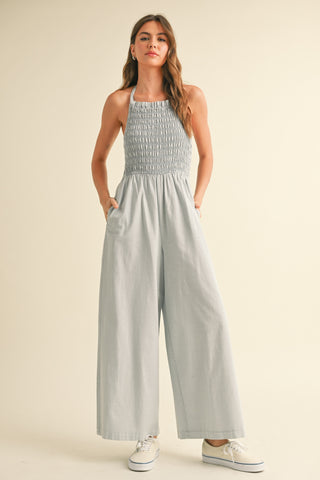 A woman wearing a gray halter jumpsuit with a smocked bodice STMT BOUTIQUE 