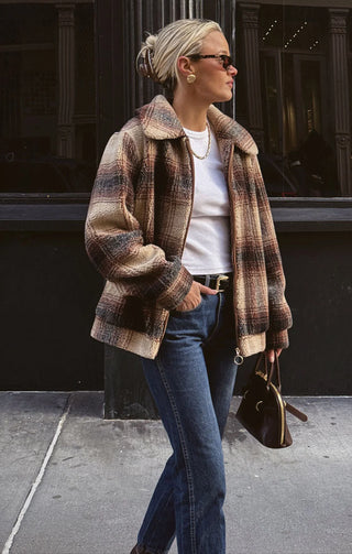 Woman wearing a plaid coat, white shirt, and blue jeans walking on a street.