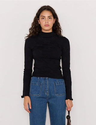 Woman wearing a black turtleneck and blue jeans against a plain background