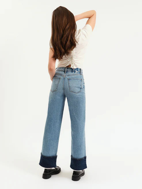 Person wearing light blue jeans with dark cuffs on a white background