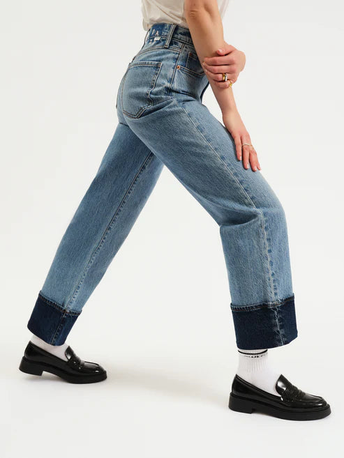 Person wearing blue jeans with rolled-up cuffs on a white background