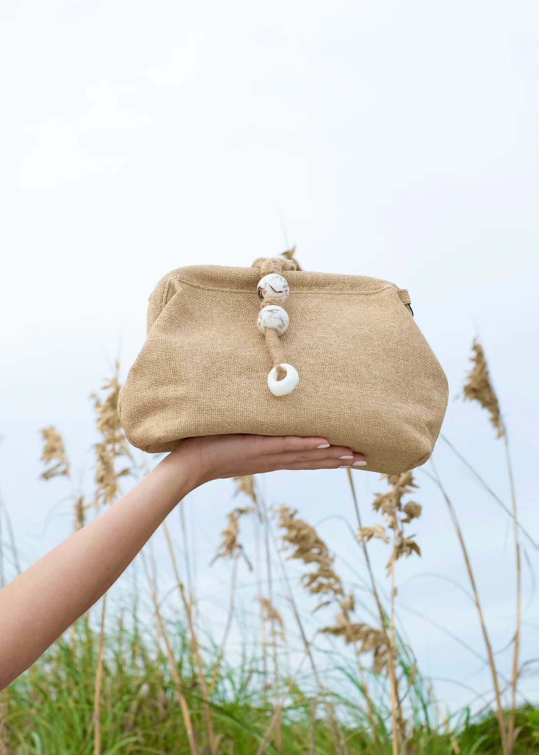 Beige clutch bag with decorative buttons held by a hand against a natural background