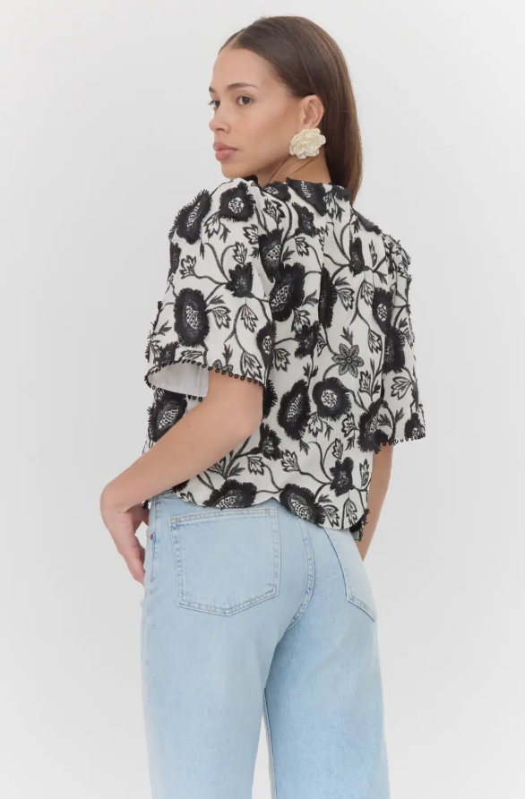 A woman wearing a black and white floral embroidered blouse STMT BOUTIQUE 