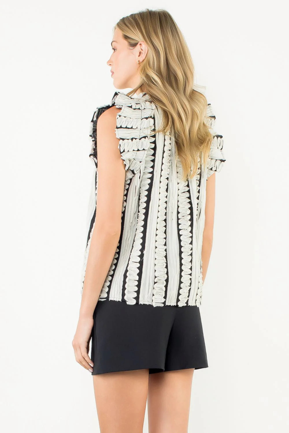 Woman wearing a sleeveless black and white patterned top with a plain background