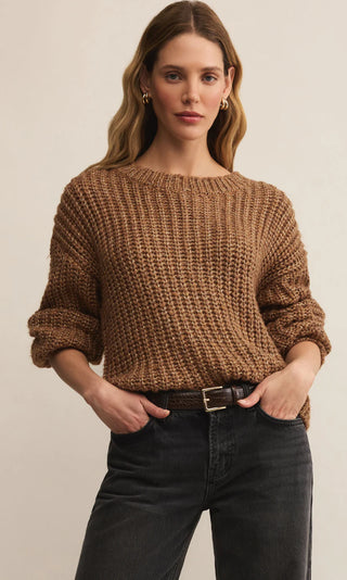 Woman wearing a brown knitted sweater and dark jeans against a beige background