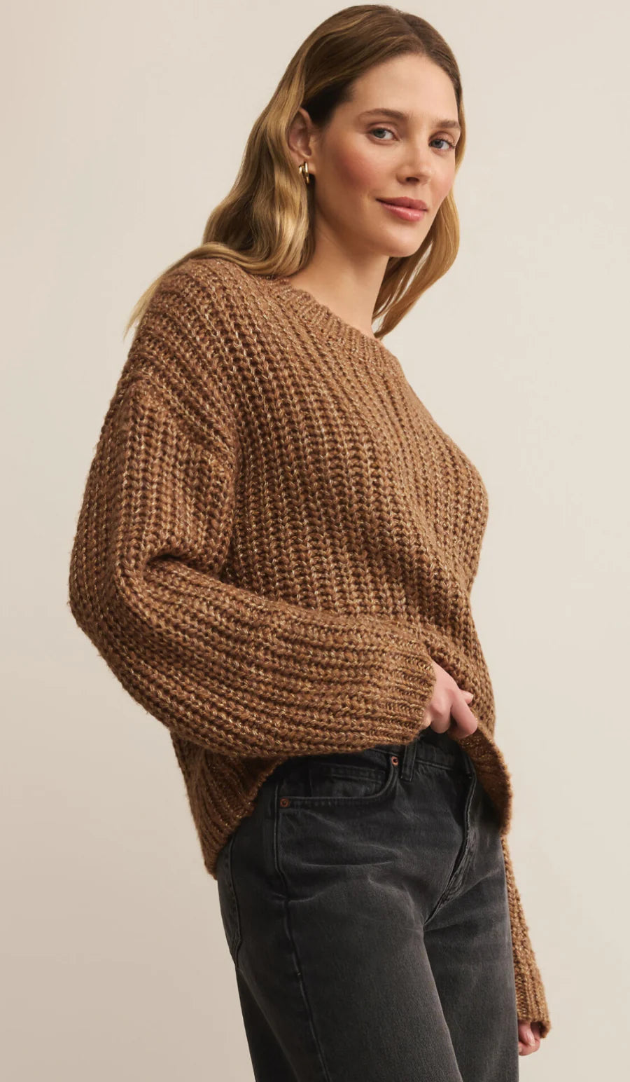 Woman wearing a brown chunky knit sweater against a plain background