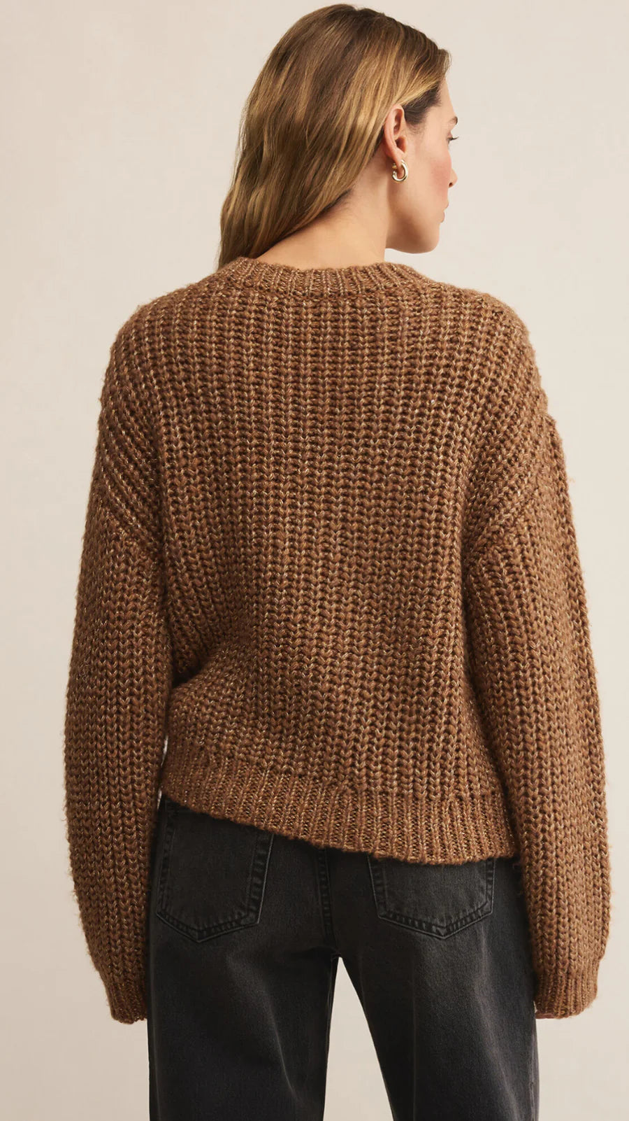 Person wearing a brown knitted sweater against a beige background