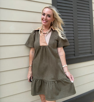 Woman wearing an olive green dress standing in front of a house.