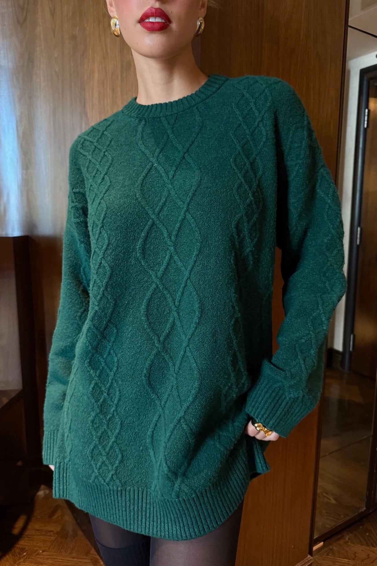 Person wearing a green cable knit sweater indoors.