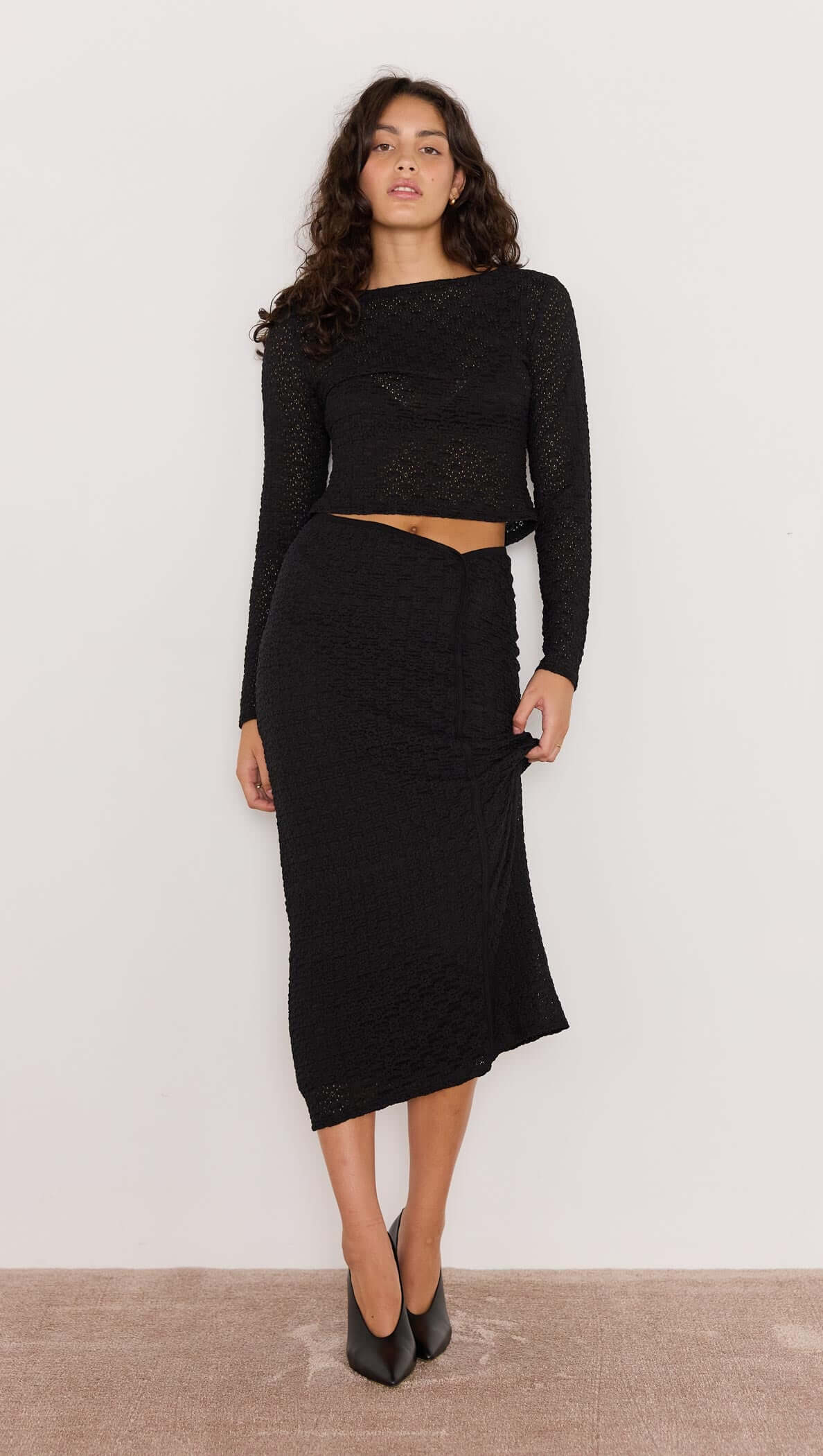 Woman wearing a black long-sleeve top and black skirt against a white background