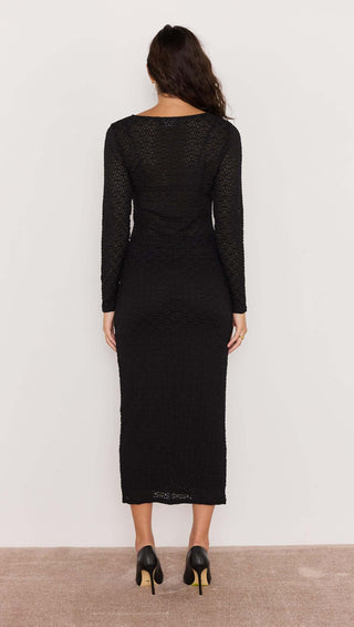 Woman wearing a black dress with long sleeves against a white background