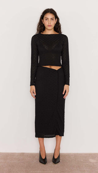 Woman wearing a black long-sleeve top and skirt set against a plain background