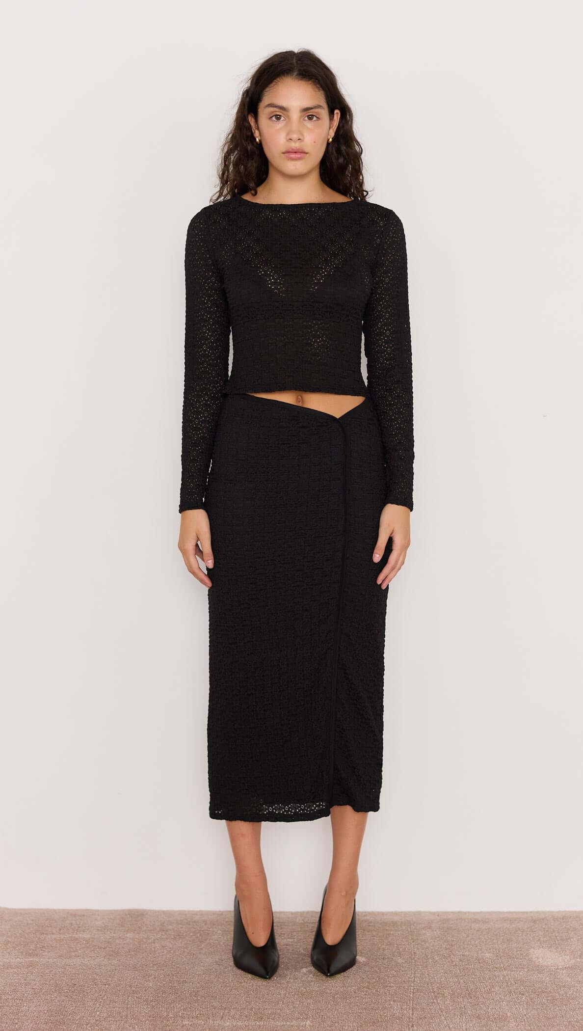 Woman wearing a black long-sleeve top and skirt set against a plain background