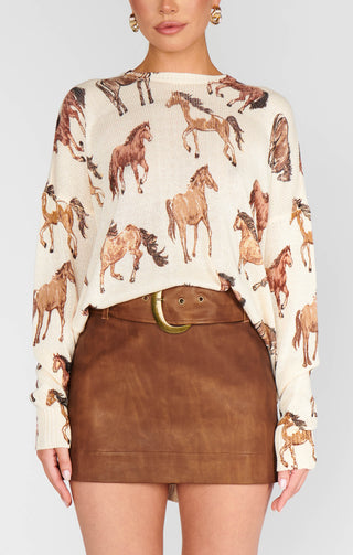 Woman wearing a sweater with horse pattern and brown leather skirt on a plain background