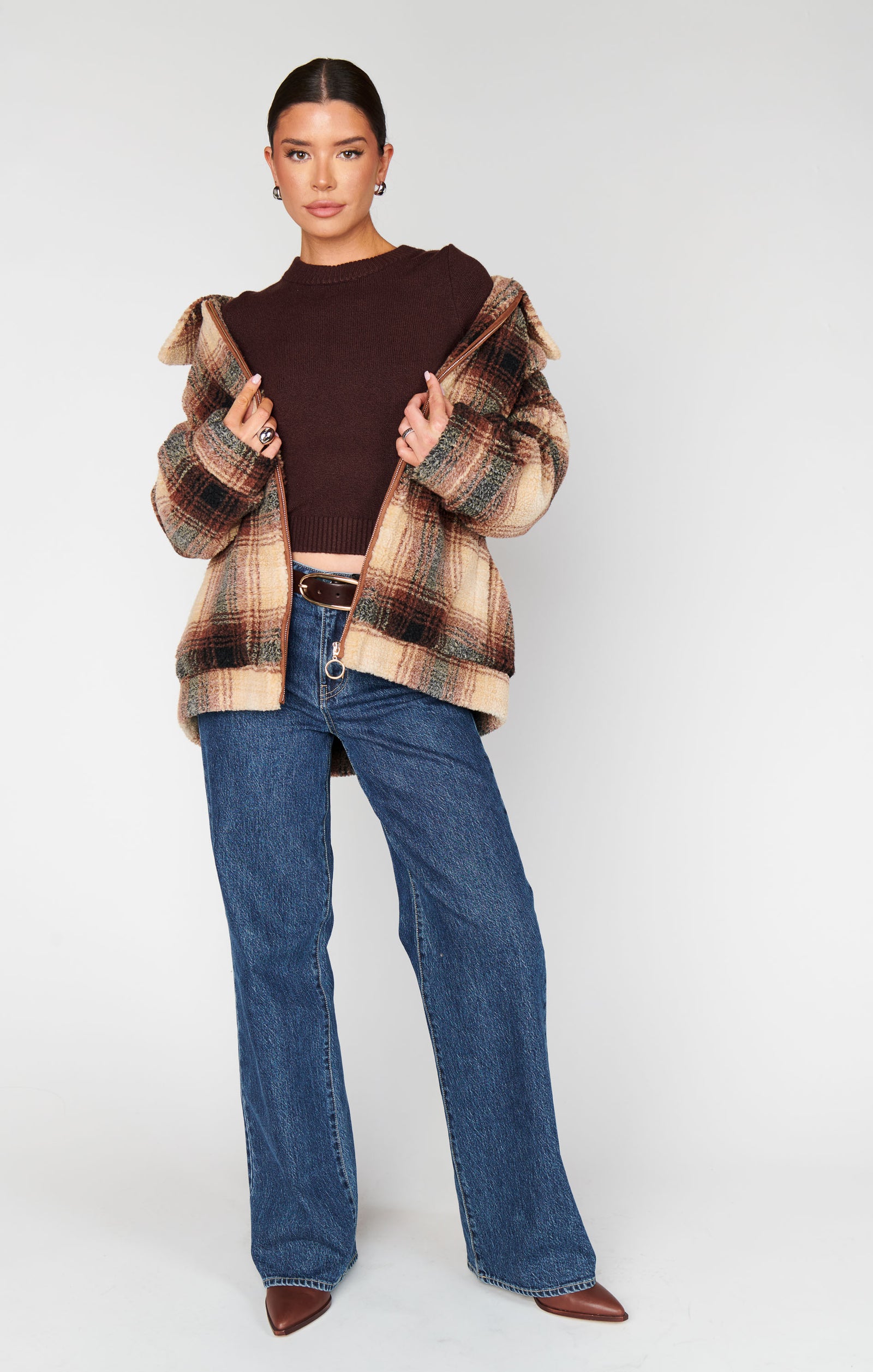 Person wearing a plaid jacket, brown top, and blue jeans on a white background