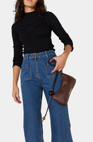 Person wearing a black long-sleeve top and blue jeans, holding a brown handbag on a white background