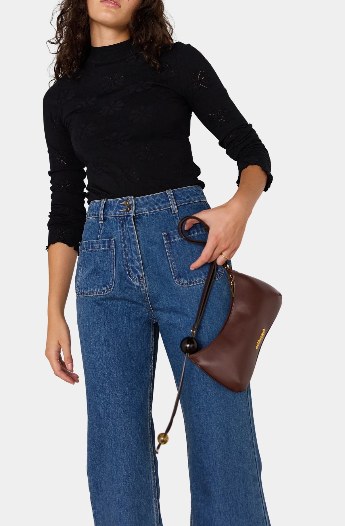 Person wearing a black long-sleeve top and blue jeans, holding a brown handbag on a white background