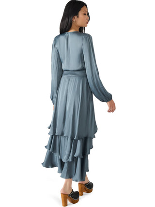 Woman wearing a long, light blue dress with ruffled layers on a white background