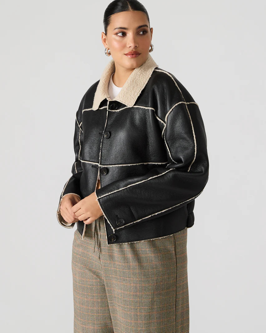 Woman wearing a black leather jacket with beige interior on a plain background