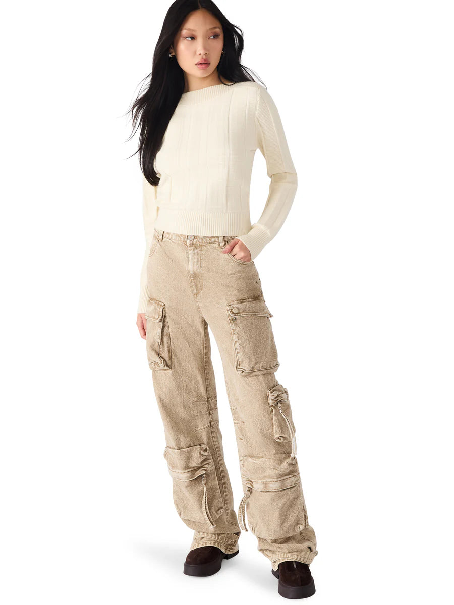 Woman wearing a cream sweater and beige cargo pants on a white background