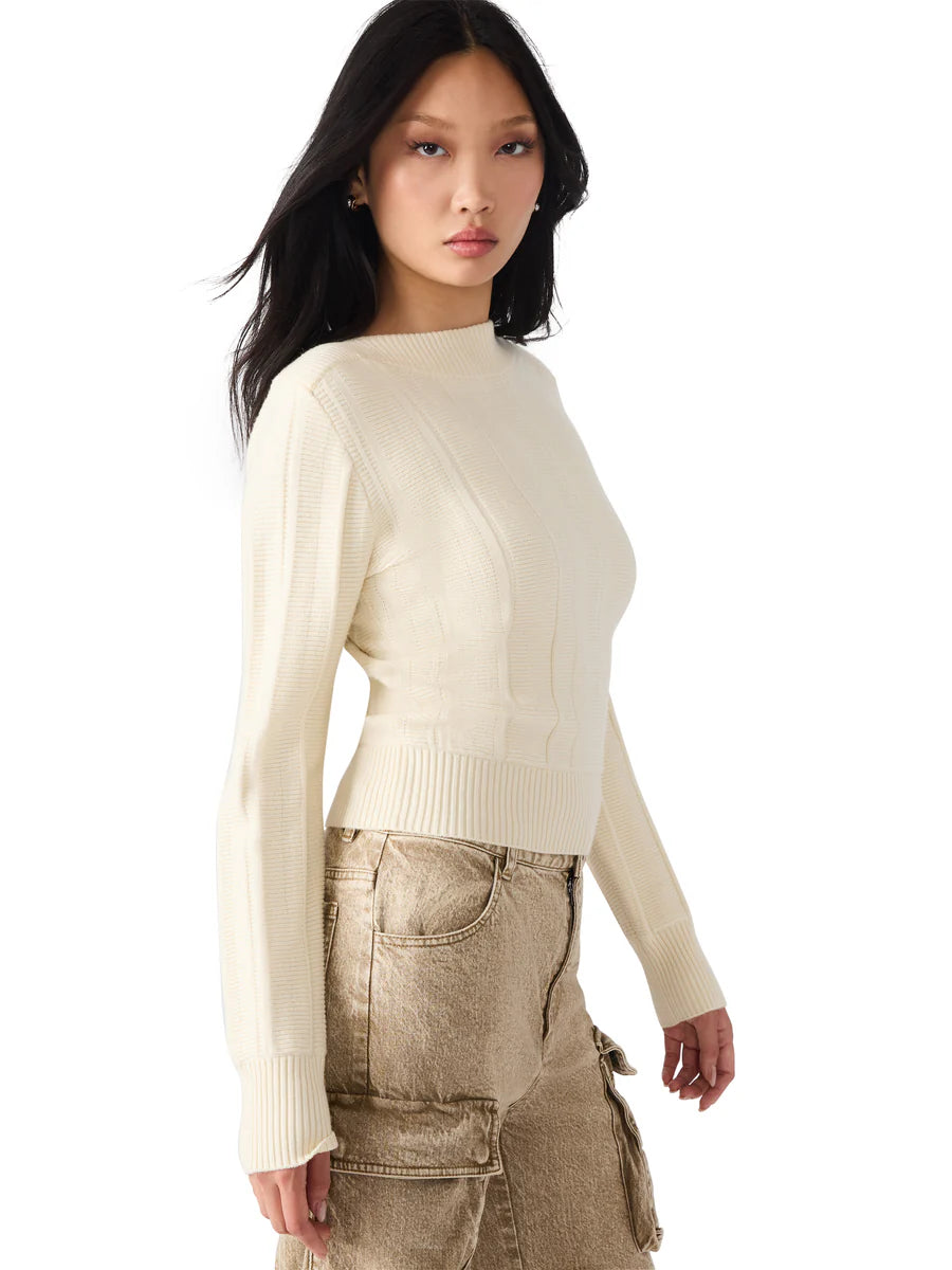 Woman wearing a cream sweater and beige pants on a white background