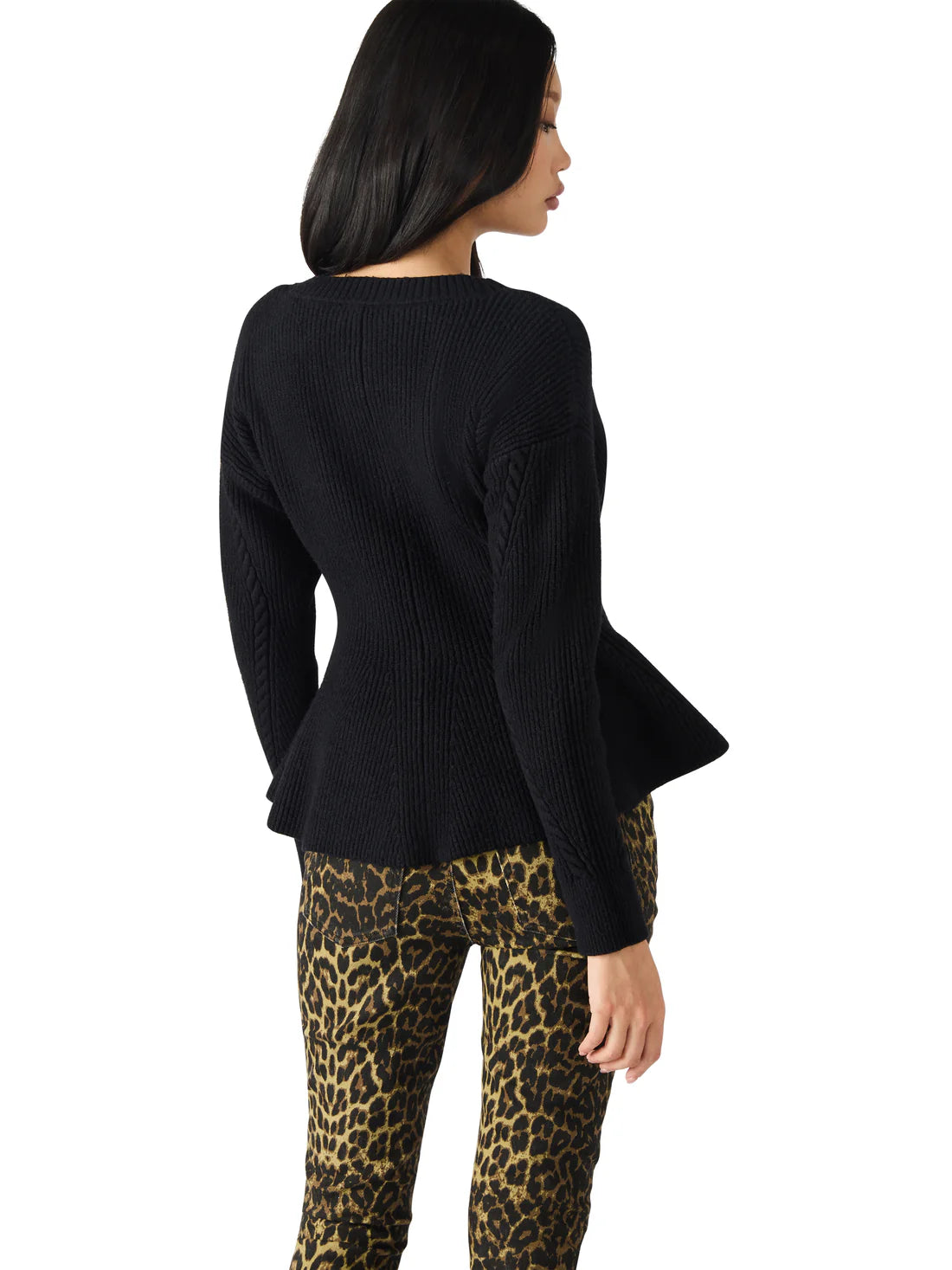 Woman wearing a black ribbed sweater and leopard print pants on a white background