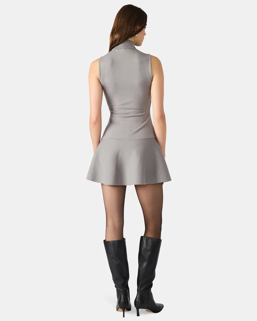 Woman wearing a gray sleeveless dress and black knee-high boots on a white background