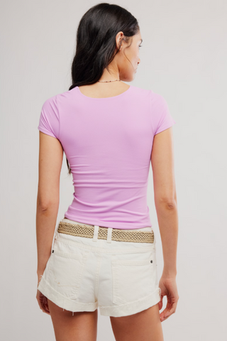 Woman wearing a pink top and white shorts with a beige belt on a plain background