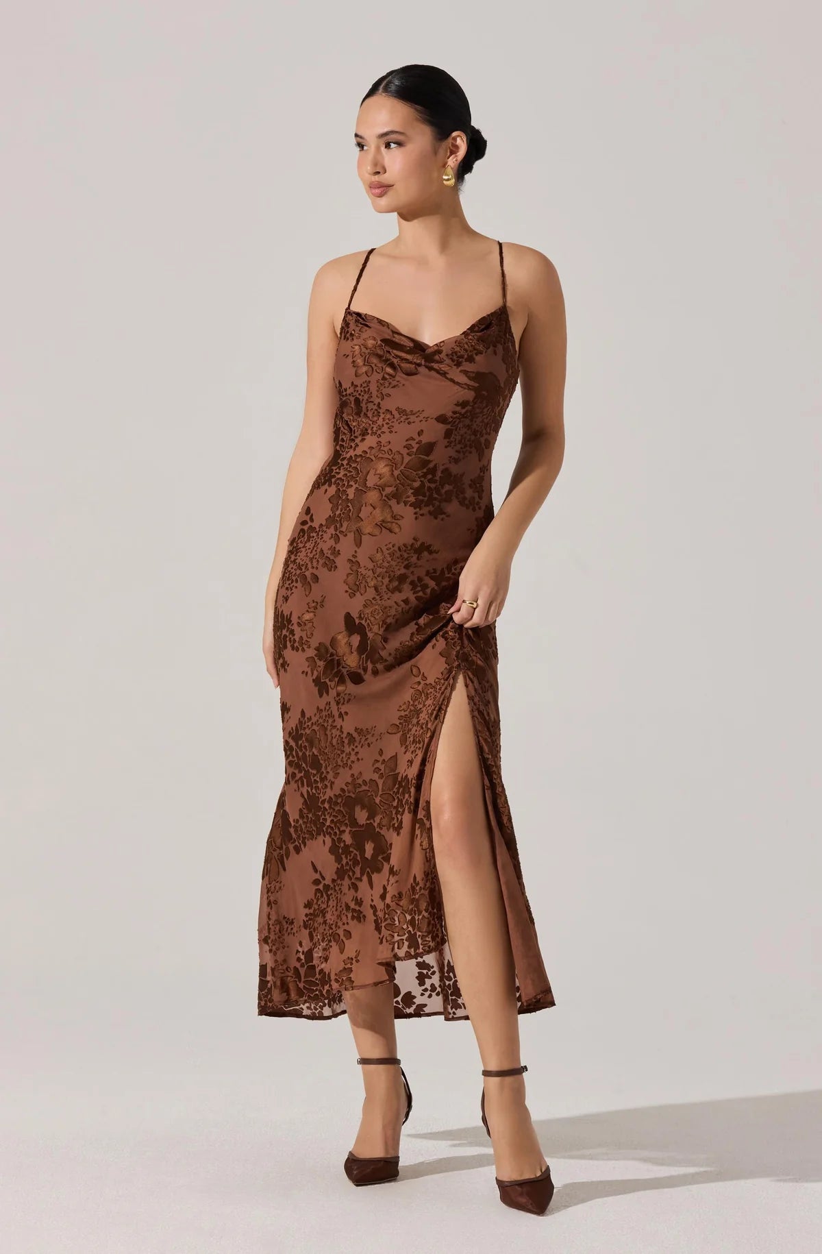 Woman in a brown lace dress standing on a wooden deck with greenery in the background