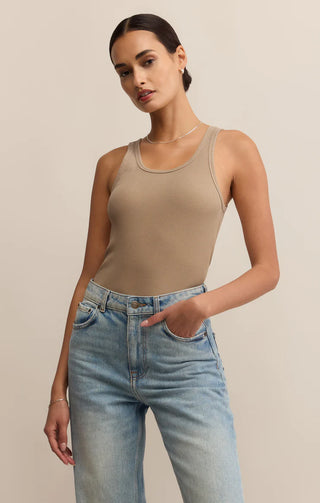 Woman wearing a beige tank top and blue jeans against a neutral background