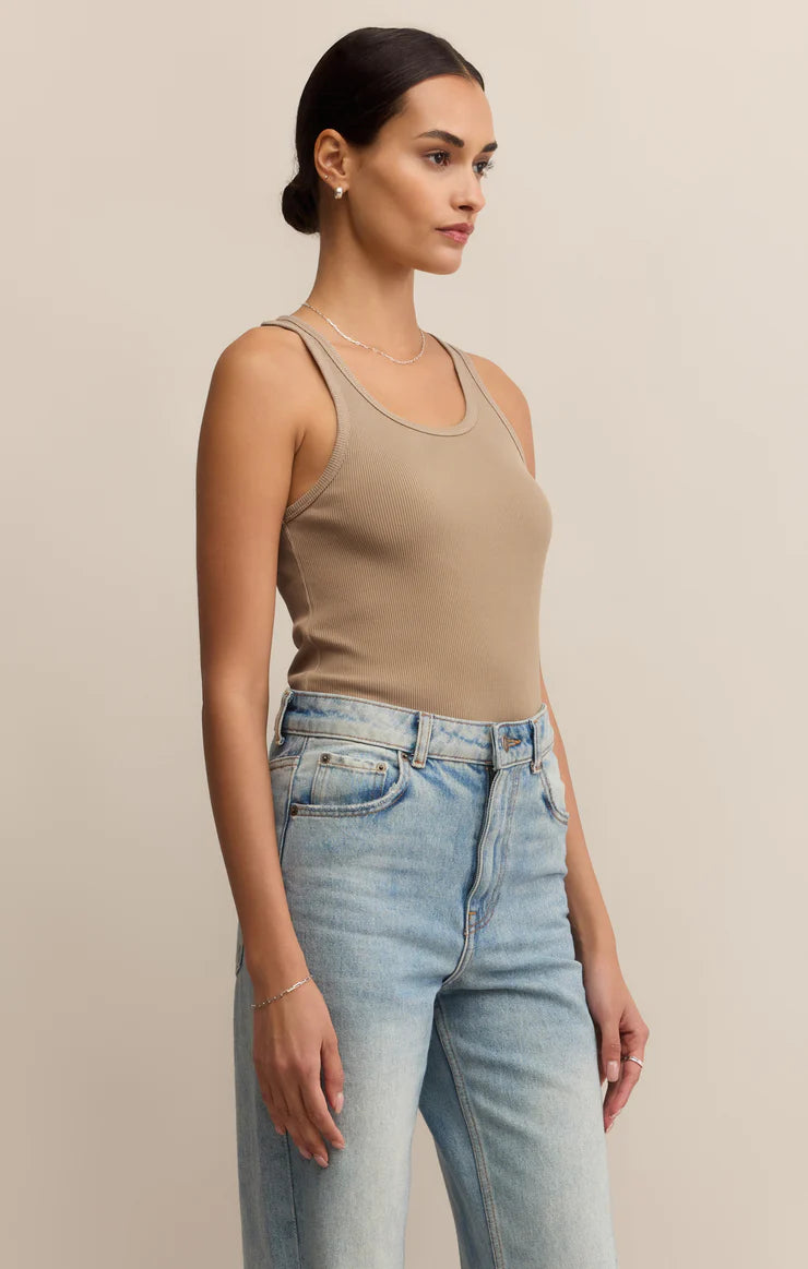 Woman wearing a beige tank top and blue jeans against a neutral background