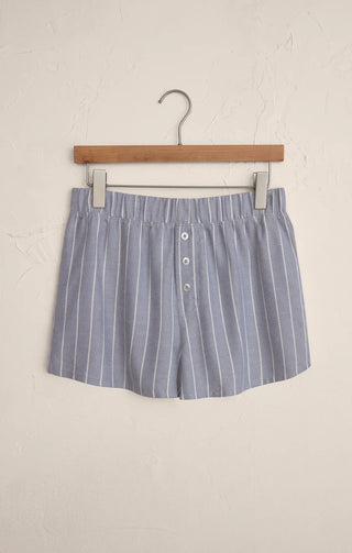 Blue and white striped shorts on a wooden hanger against a beige background