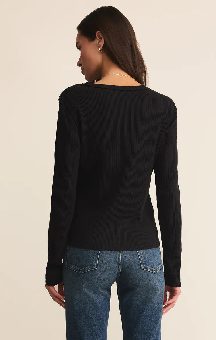 Person wearing a black long-sleeve top and blue jeans on a beige background