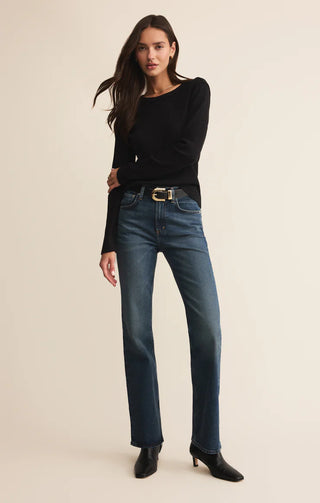 Woman wearing a black top and blue jeans on a beige background