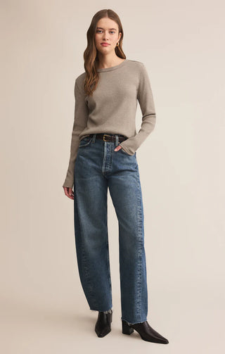 Woman wearing a beige sweater and blue jeans on a beige background