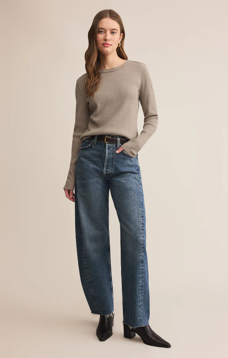 Woman wearing a beige sweater and blue jeans on a beige background