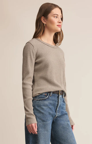 Woman wearing a beige sweater and blue jeans against a plain background
