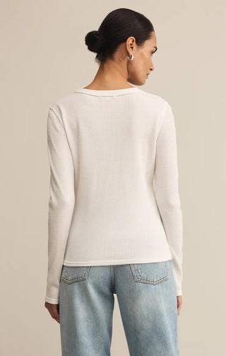 Person wearing a white ribbed sweater and light blue jeans against a beige background