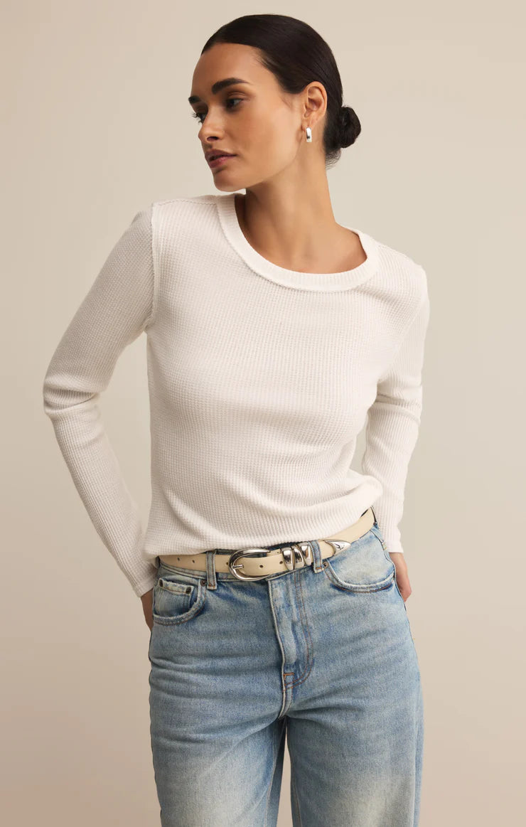Woman wearing a white long-sleeve top and blue jeans on a beige background