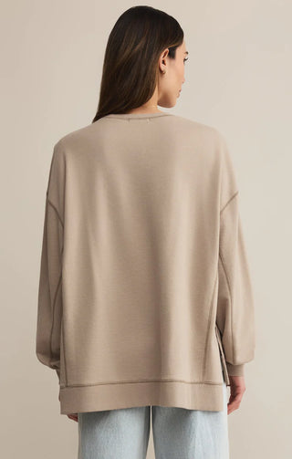 Person wearing a beige sweater and light blue jeans on a beige background