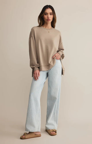 Woman wearing a beige sweater and light blue jeans on a beige background