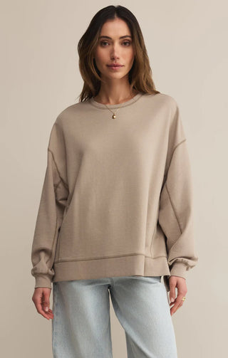Woman wearing a beige sweatshirt and light blue jeans against a beige background