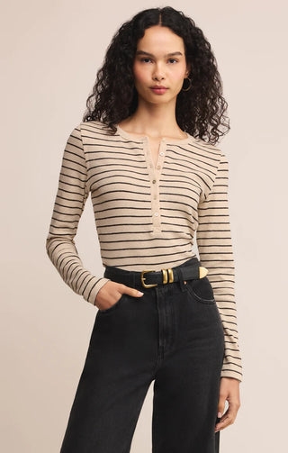 Woman wearing a striped long-sleeve top and black pants on a beige background