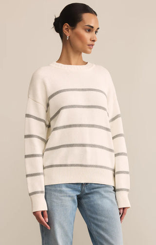 Woman wearing a cream and gray striped sweater with light blue jeans on a beige background