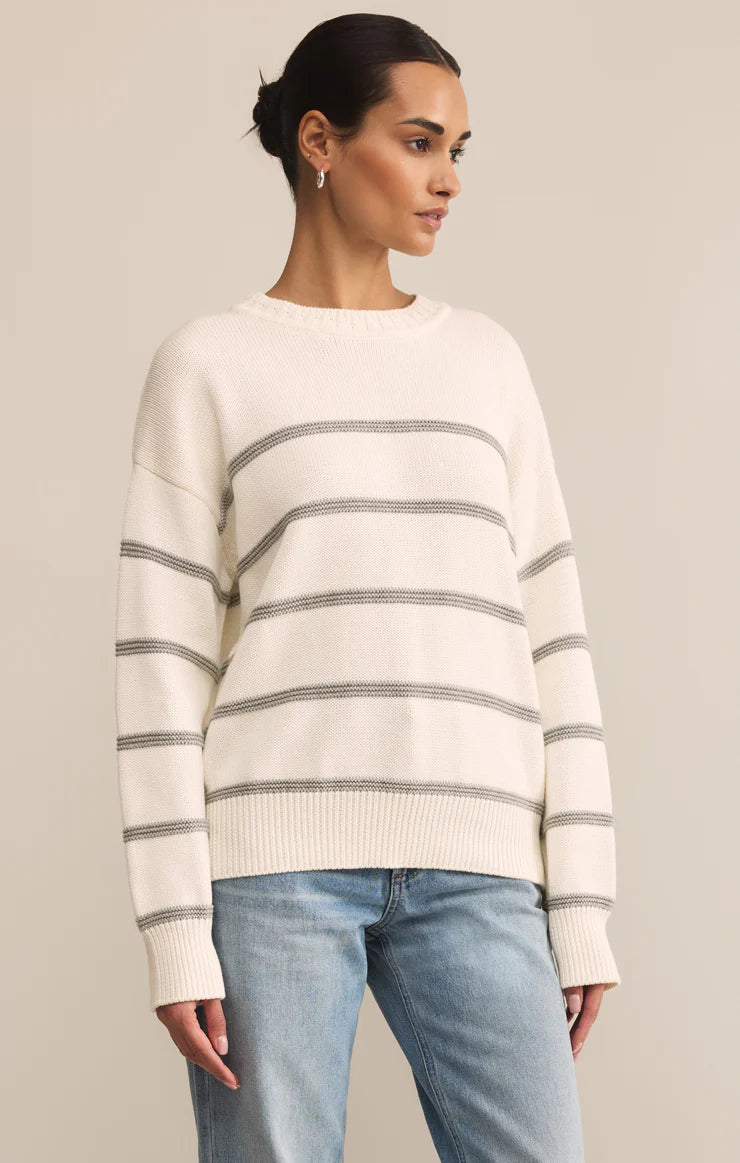 Woman wearing a white sweater with gray stripes and blue jeans on a beige background