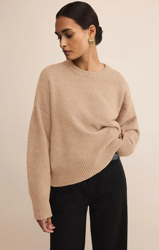 Woman wearing a beige sweater and black pants against a beige background